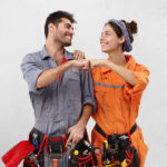 Teamwork and cooperation concept. Studio shot of young European male and female technicians in overalls standing at blnak wall and making fist bump gesture celebrating good results and success at work